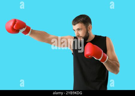 Sportlicher junger Mann in Boxhandschuhen auf blauem Hintergrund Stockfoto