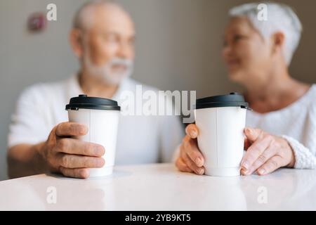 Nahaufnahme selektiver Fokus von Seniorenpaaren, die gute Zeit miteinander verbringen, Kaffeetassen zum Mitnehmen halten und sich in einem gemütlichen Café unterhalten Stockfoto