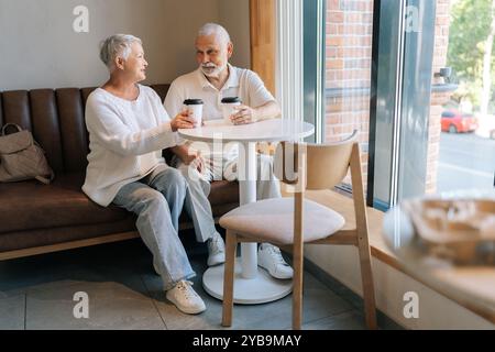 Porträt eines älteren Ehepaares, das Kaffee in einem gemütlichen Café genießt, sich im sonnendurchfluteten Raum fröhlich unterhält und Liebe und Zufriedenheit ausstrahlt. Glückliches Rentenleben erfüllt Stockfoto