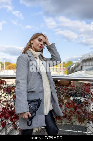 Nahaufnahme Porträt einer schönen lächelnden Frau in weißem Wollstrickpullover und Mantel draußen, gegen modernes Gebäude, Geschäftsfrau Stockfoto