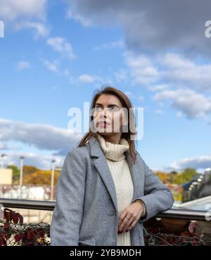 Nahaufnahme Porträt einer schönen lächelnden Frau in weißem Wollstrickpullover und Mantel draußen, gegen modernes Gebäude, Geschäftsfrau Stockfoto