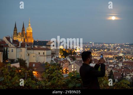 Prag, Tschechische Republik. Oktober 2024. Der Mann fotografiert mit seinem Smartphone den Supermond über dem Panorama des historischen Teils der tschechischen Hauptstadt Prag. Der historische Teil von Prag ist Teil des UNESCO-Weltkulturerbes. Der Vollmond im Oktober, auch bekannt als der Jägermond, ist der größte und hellste Supermond in diesem Jahr. (Foto: Tomas Tkacik/SOPA Images/SIPA USA) Credit: SIPA USA/Alamy Live News Stockfoto