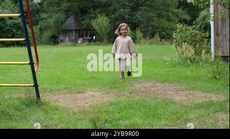 Glückliches kleines Mädchen lächelt und rennt durch den Hof eines Landhauses. Landleben. Das Mädchen läuft im Hof ihres Hauses. Glückliche Kindheit Stockfoto