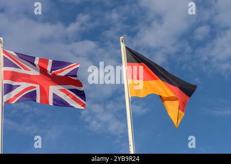 Zwei leuchtende Flaggen, die das Vereinigte Königreich und Deutschland repräsentieren, winken sanft vor einem Hintergrund aus flauschigen Wolken und hellblauem Himmel und symbolisieren Freunde Stockfoto