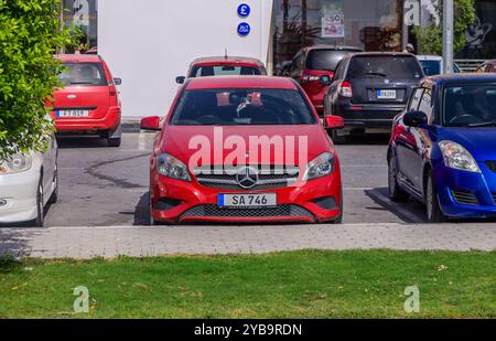 Ein hellrotes Luxusauto parkt an einem sonnigen Tag auf einem belebten Parkplatz, umgeben von verschiedenen anderen Fahrzeugen, die moderne Automobile zeigen Stockfoto