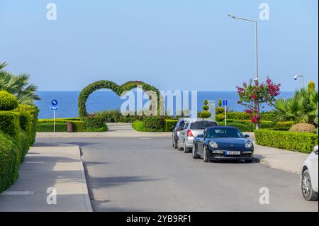 Eine malerische Küstenstraße zeigt gut gepflegte Hecken und farbenfrohe Blumen, die in einem einzigartigen herzförmigen Bogen münden, der das ruhige Meer umrahmt Stockfoto