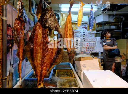 Getrocknete Fische hängen an einem Marktstand im Sankaku Markt, alias Otaru Dreieck Markt, mit einer weiblichen Kundin hinter Otaru.Hokkaido, Japan Stockfoto