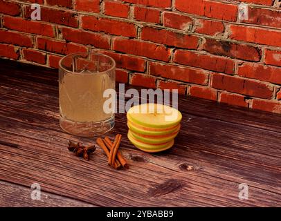 Ein Kristallglas Apfellikör, neben reifem Obst und Zimt mit Anis auf einem Holztisch. Nahaufnahme. Stockfoto