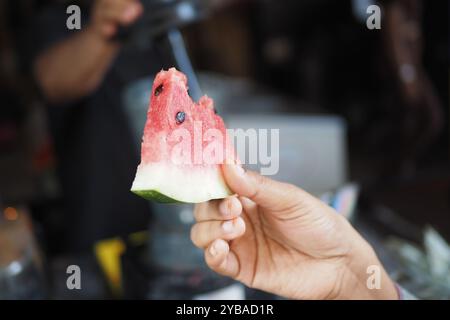 Ein frisches Stück Wassermelone, gehalten von einer Hand vor einem lebendigen und lebendigen Hintergrund Stockfoto