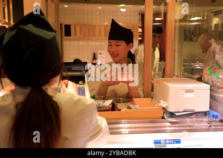 Lächelnde Angestellte in Uniform im Bestellfenster eines Sushi-Restaurants in Kyoto. Japan Stockfoto