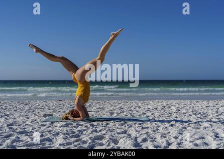 Eine ruhige und malerische Szene mit einem wunderschönen blonden Model, das am frühen Morgen Yoga am Strand praktiziert Stockfoto