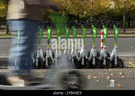 Verkehr, Mobilität, Bewegungsunschärfe, Rollerfahrer und aufgereihte E-Scooter des Anbieters Lime im Herbst auf einer Straße in Berlin, Deutschland, Europa Stockfoto