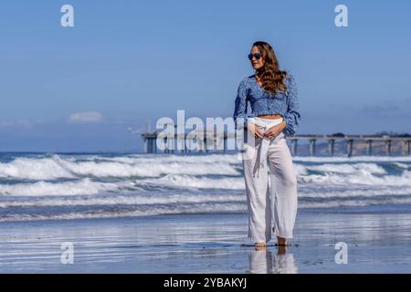Atemberaubende Frau sonnt sich in der Nähe eines Piers, unter klarem blauem Himmel und genießt die Ruhe eines perfekten Tages am Meer Stockfoto