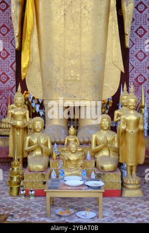 Kleine goldfarbene Buddha-Statuen umgaben die Füße der großen stehenden Buddha-Statue im Tempel Wat Sen Souk Haram. Luang Prabang, Laos Stockfoto