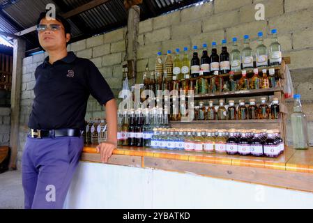 Ein männlicher Reiseleiter stellt den Besuchern destillierte laotische Reisbrände im Dorf Ban Xang Hai, auch bekannt als Whisky Village, vor. In der Nähe von Luang Prabang, Laos Stockfoto