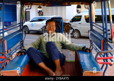 Ein männlicher Tuk-Tuk-Fahrer macht eine Pause, während er auf der Straße von Vientiane, Laos, auf Kunden wartet Stockfoto