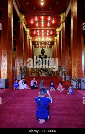 Eine Familie, die ihre Fotos vor Phra Ong TEU, der großen bronzenen Buddha-Statue, in Begleitung eines stehenden Buddha im Haupttempelsaal des Wat Ong TEU Tempels (Tempel des schweren Buddha), machen lässt. Vientiane, Laos Stockfoto