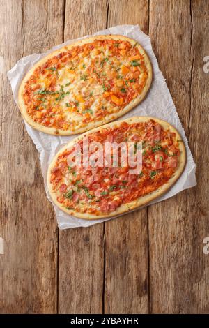 Ovale Portion Pizza von zwei Arten, drei Käse und Käse mit Schinken in Nahaufnahme auf Pergament auf einem Holztisch. Vertikale Draufsicht von oben Stockfoto