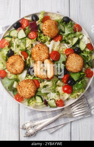 Gebratener Ziegenkäsesalat mit Tomaten, Oliven, Gurken und Salat aus der Nähe auf dem Teller auf dem Tisch, vertikale Draufsicht von oben Stockfoto