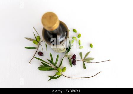 Blick von oben auf eine Flasche Olivenöl mit grünen und schwarzen Oliven auf Zweigen und losen grünen Oliven, isoliert in einem weißen Hintergrund. Stockfoto