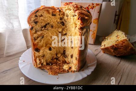 Ein in Scheiben geschnittener Panettone-Weihnachtskuchen auf einem Teller mit dem Paket und die Scheibe im Hintergrund. Stockfoto