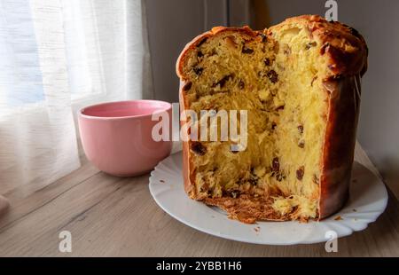 Ein italienischer Panettone, Weihnachtskuchen, mit einer Scheibe geschnitten, auf einem Sideboard mit einer Tasse Tee oder Kaffee. Stockfoto