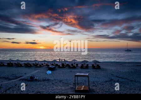 Kathisma Beach, Insel Lefkada, Griechenland, mit Sonnenliegen, Sonnenschirmen, und Touristen genießen die atemberaubenden letzten Sonnenstrahlen, während die Sonne unter dem Meereshorizo untergeht Stockfoto