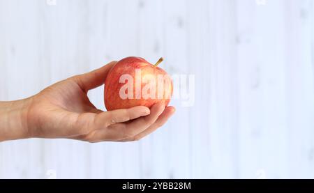Reifer Apfel in der Hand der Frau auf hellem hölzernem Hintergrund. Nahaufnahme der Hand mit Apfel. Konzept der gesunden Ernährung, Vitamine und Ernährung. Obst. Weiße Buchse Stockfoto