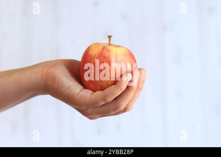 Reifer Apfel in der Hand der Frau auf hellem hölzernem Hintergrund. Nahaufnahme der Hand mit Apfel. Konzept der gesunden Ernährung, Vitamine und Ernährung. Obst. Weiße Buchse Stockfoto