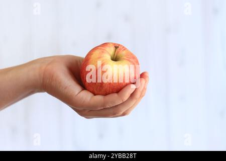 Reifer Apfel in der Hand der Frau auf hellem hölzernem Hintergrund. Nahaufnahme der Hand mit Apfel. Konzept der gesunden Ernährung, Vitamine und Ernährung. Obst. Weiße Buchse Stockfoto
