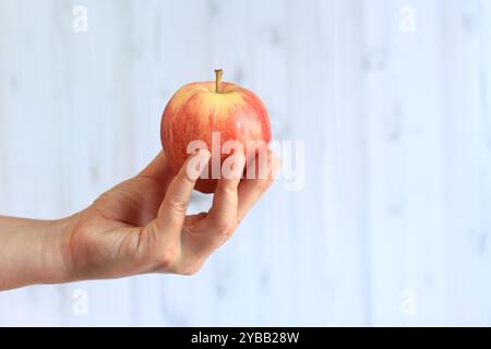 Reifer Apfel in der Hand der Frau auf hellem hölzernem Hintergrund. Nahaufnahme der Hand mit Apfel. Konzept der gesunden Ernährung, Vitamine und Ernährung. Obst. Weiße Buchse Stockfoto