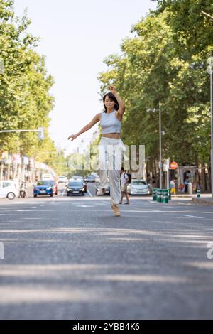 Sorglose Frau tanzt glücklich in einer verkehrsfreien Straße und genießt urbane Freiheit und Freude an einem sonnigen Sommertag Stockfoto
