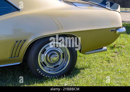 Nahaufnahme des Hinterrads und des auspuffrohrs eines goldenen chevrolet camaro z28, der auf einem grasbewachsenen Feld geparkt ist Stockfoto