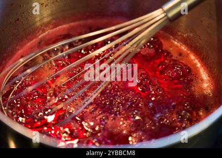 Nahaufnahme eines kochenden Candy Apple Sirup in einem Metalltopf mit einem Schneebesen. Stockfoto