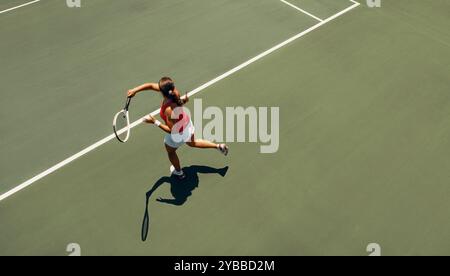 Luftaufnahme einer Tennisspielerin in Bewegung, die während eines Spiels auf einem Platz im Freien einen Vorhand-Schlag ausführt. Stockfoto