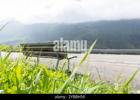 Holzbank auf der Seite einer Schweizer Bergstraße. Niemand schwitzt, aber die Aussicht ist romantisch. Er sieht um und hinter dem grünen Berggras Stockfoto