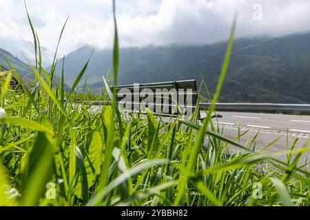 Holzbank auf der Seite einer Schweizer Bergstraße. Niemand schwitzt, aber die Aussicht ist romantisch. Er sieht um und hinter dem grünen Berggras Stockfoto