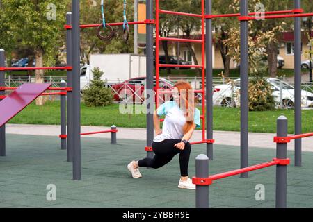 Frau, die Ausfallschritte während des Trainings im Freien auf dem Spielplatz macht, zeigt Konzentration und Hingabe. Stockfoto