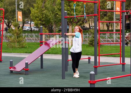 Frau lehnt sich auf Fitnessringe auf dem Spielplatz im Freien und lächelt während des Trainings. Stockfoto