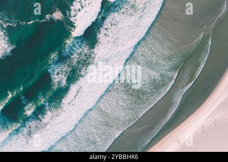 Meereswellen kommen am Ufer eines schäumenden Strandes an, Blick von oben mit Drohne bei Sonnenaufgang. Stockfoto