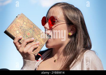 Eine junge Frau mit seitlichem Blick, die draußen ein Buch beißt Stockfoto