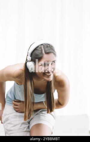 Die junge Frau lacht zu Hause glücklich, hört Musik mit Kopfhörern und genießt einen unbeschwerten Moment der Freude und des Vergnügens in ihrem gemütlichen Wohnzimmer Stockfoto
