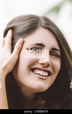 Die junge Frau berührt glücklich ihr Haar, lächelt mit einem fröhlichen Ausdruck drinnen, strahlt Freude und natürliche Schönheit aus Stockfoto