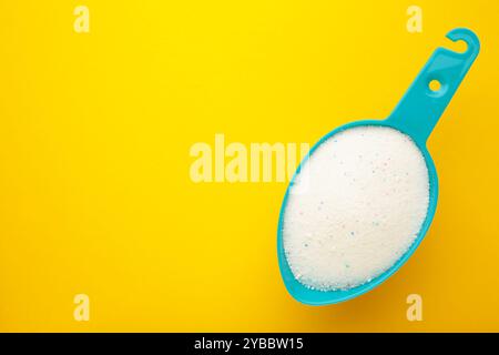 Waschmittelpulver für Waschmaschine in Kunststoffschaufel auf gelbem Hintergrund. Draufsicht Stockfoto