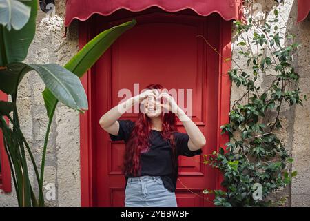 Junge Frau mit langen roten Haaren, die Herz mit Fingern zeigt Stockfoto