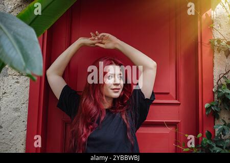 Eine junge Frau mit langen roten Haaren, die sich an der roten Tür ausdehnen Stockfoto