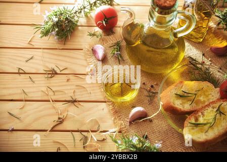 Holztisch mit Behältern mit ätherischem Rosmarinöl und gewürzten Brotscheiben und natürlichen Lebensmitteln, die mit Rosmarinzweigen verziert sind. Obere Höhe Stockfoto
