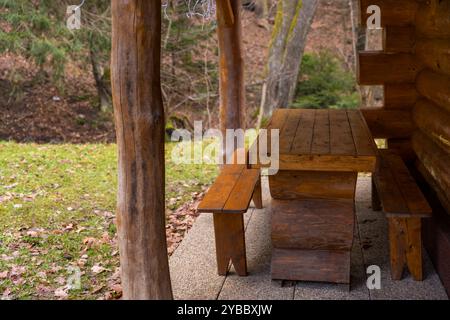 Rustikaler Holztisch mit zwei Bänken in der Nähe einer Blockhütte an einem bewölkten, schneefreien Wintertag in einem Wald. Stockfoto
