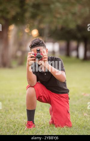 Junge kniend auf dem Gras und macht ein Foto mit seiner Kamera Stockfoto