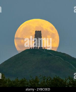 Glastonbury, Somerset, Großbritannien. Oktober 2024. Wetter in Großbritannien. Der volle Supermond der Hunters schwingt den St Michael’s Tower am Glastonbury Tor in Somerset, während er sich hinter dem Wahrzeichen erhebt, während sich eine Menschenmenge auf dem Hügel versammelt, um zu beobachten. Bildnachweis: Graham Hunt/Alamy Live News Stockfoto